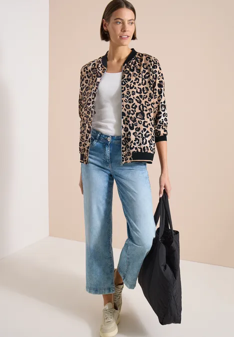 Femme portant une veste léopard, un top blanc, jean évasé, baskets vertes et un sac en tissu noir.