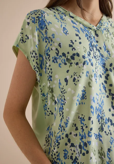 Eine hellgrüne Bluse mit abstrakten blauen Tupfen.