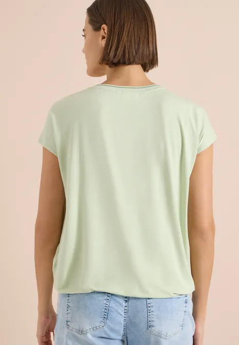 Kurzarm Blusenshirt mit Strukturmix raw matcha lime Frau von hinten in hellgrünem T-Shirt und Jeans vor hellem Hintergrund.