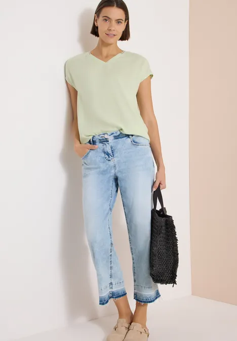 Kurzarm Blusenshirt mit Strukturmix raw matcha lime Eine Frau steht vor hellem Hintergrund in grüner Bluse, weiten, gekürzten Jeans und hält eine schwarze Tasche.
