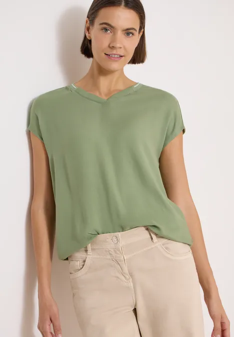 Kurzarm Blusenshirt mit Strukturmix deep matcha green Frau trägt lockeres grünes T-Shirt mit Cap-Ärmeln und beigefarbener Hose.