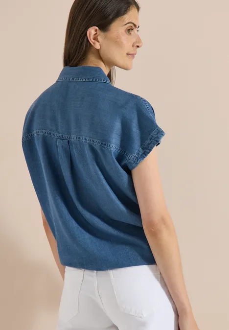 Chemisier à épaules tombantes, effet denim mid blue wash Eine Frau trägt eine kurzärmlige Jeansbluse und weiße Hose, Rückenansicht vor hellem Hintergrund.