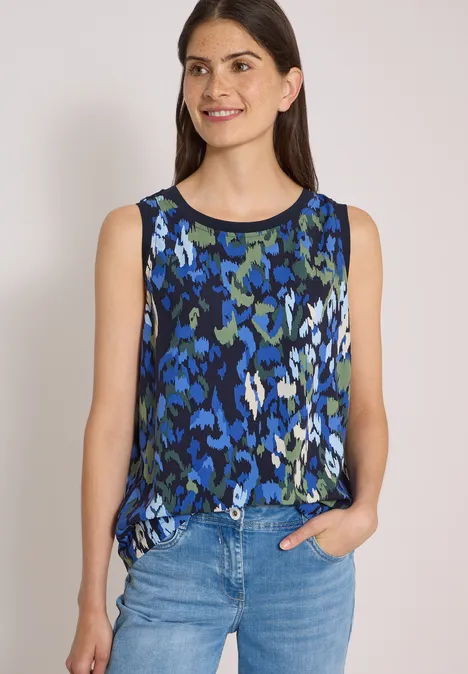 Ärmelloses Top mit blau-grünem, abstraktem Blumenmuster, kombiniert mit blauen Jeans.