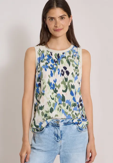 Ärmelloses weißes Top mit blau-grünem Blumenmuster und Rundhalsausschnitt, kombiniert mit Jeans.