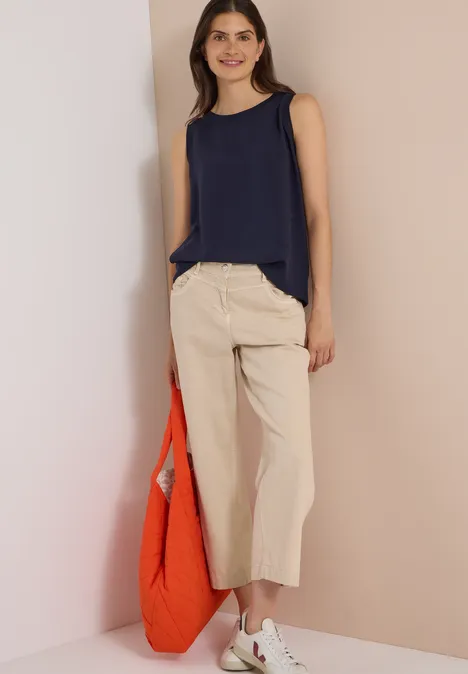 Blusentop mit Rundhals und Rippdetails urban dark blue Frau in dunkelblauem Top und weiten, beigen Culotte-Hosen hält eine orange Tasche.