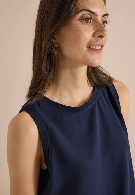 Blusentop mit Rundhals und Rippdetails urban dark blue Eine Frau mit dunklem ärmellosem Top, leichtem Make-up und braunen Haaren, blickt seitlich und lächelt.
