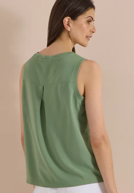 Blusentop mit Rundhals und Rippdetails deep matcha green Eine Frau trägt ein ärmelloses grünes Top und steht seitlich vor beigem Hintergrund.