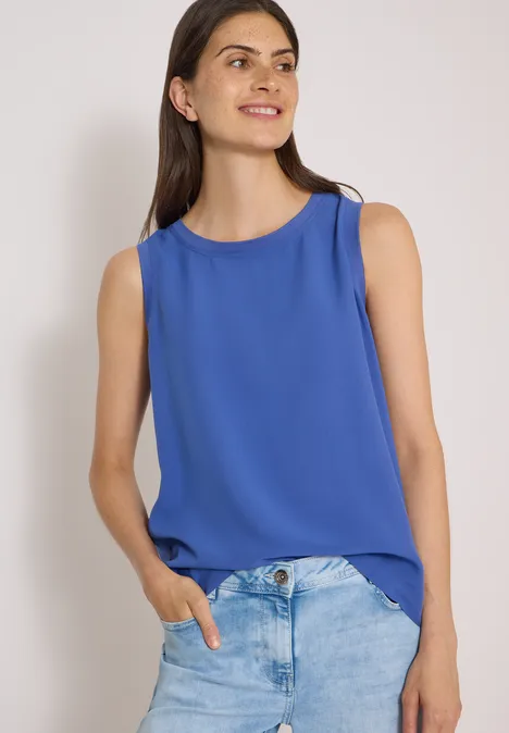 Blusentop mit Rundhals und Rippdetails deep river blue Frau trägt blaues ärmelloses Top und helle Jeanshose, lächelnd.