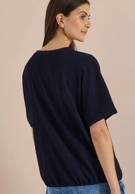 Dropped Shoulder Blusenshirt in Unifarbe urban dark blue Frau im Profil trägt dunkelblaues T-Shirt vor neutralem Hintergrund.