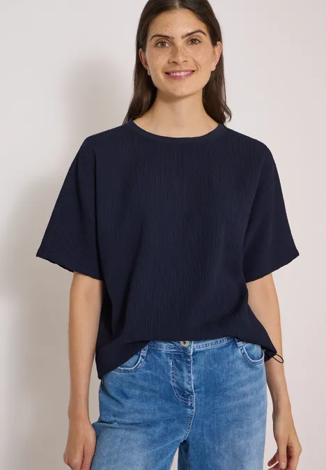 Dropped Shoulder Blusenshirt in Unifarbe urban dark blue Eine lächelnde Frau in dunkelblauem T-Shirt und Jeans vor weißem Hintergrund.