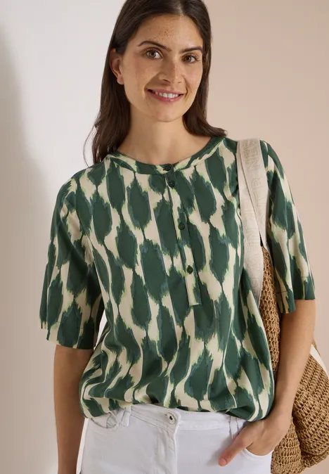 Kurzarm Bluse mit Rundhals und Print vanilla white Lächelnde Frau in grün-weißer gemusterter Bluse, weißer Hose und Korbtasche vor hellem Hintergrund.