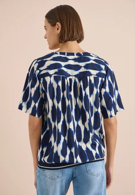 Kurzarm Bluse mit Rundhals und Print urban dark blue Rückenansicht einer Frau mit kurz geschnittenem Haar, die ein blau-weiß gemustertes Top und hellblaue Jeans trägt.