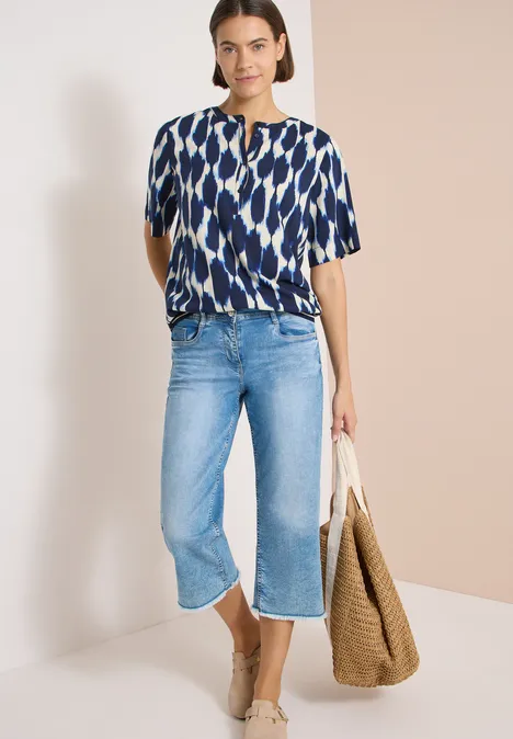 Kurzarm Bluse mit Rundhals und Print urban dark blue Frau mit gemustertem Oberteil, weiten blauen Culotte-Jeans und großem Korbtasche.