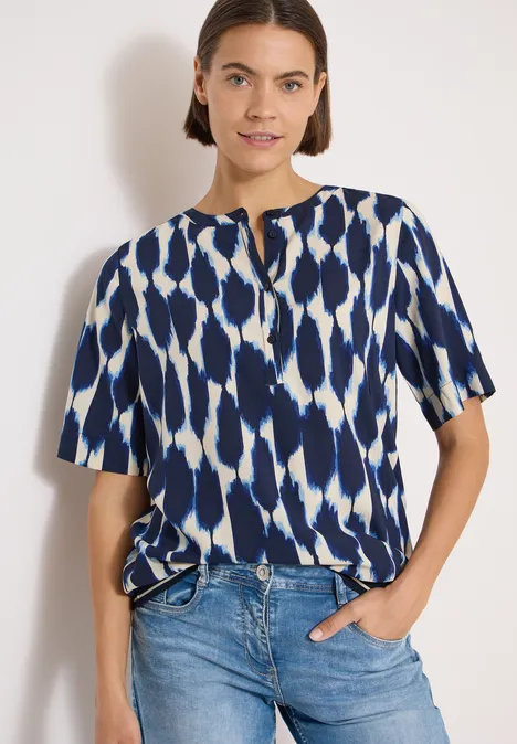Kurzarm Bluse mit Rundhals und Print urban dark blue Eine Person in Jeans und locker geschnittener Bluse mit blau-weißem Muster vor hellem Hintergrund.