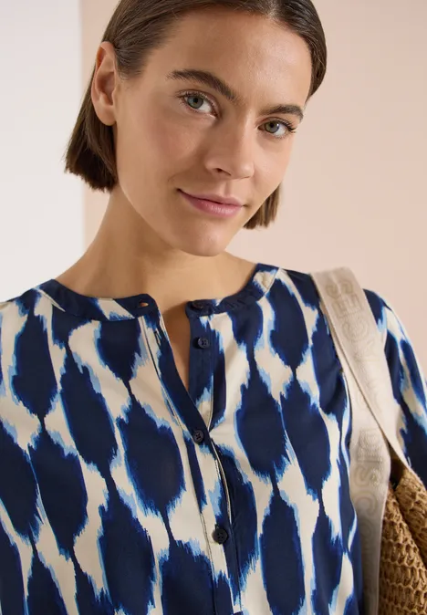 Kurzarm Bluse mit Rundhals und Print urban dark blue Frau mit Kurzhaarfrisur trägt blau-weiß gemustertes Oberteil und eine Strohtasche.