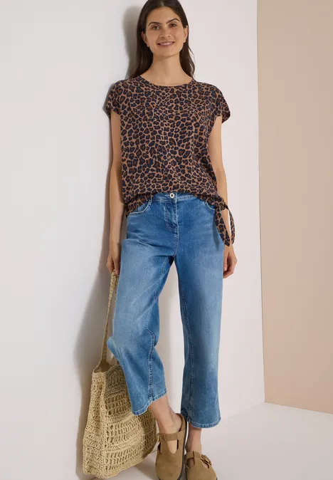 Eine Frau trägt ein gepunktetes Shirt, weite blaue Jeans, Keilsandalen und hält eine geflochtene Tasche.