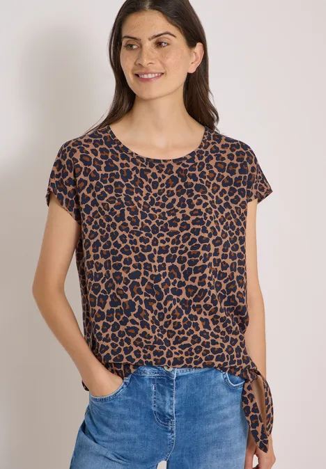Frau in braun-schwarzem Leoparden-T-Shirt mit seitlicher Schleife und blauen Jeans.