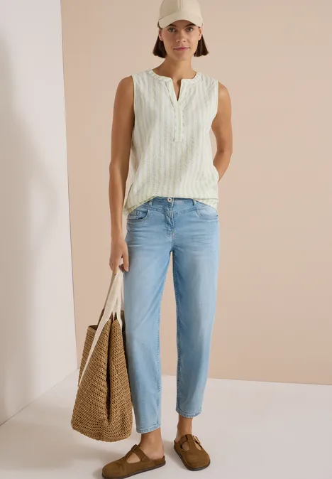 Seersucker Blusentop mit Streifen raw matcha lime Model trägt beige Cap, weiß-gemustertes Top, hellblaue Jeans, braune Loafers und Korbtasche.