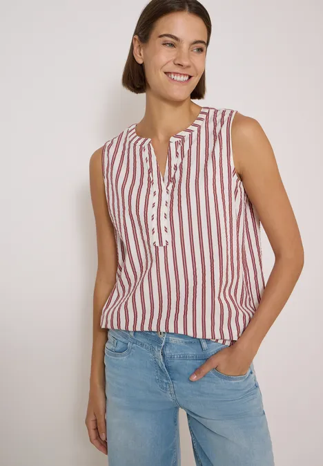 Seersucker Blusentop mit Streifen russet red Frau mit kurzem braunem Haar trägt ärmelloses Top mit roten Streifen und blaue Jeans, lächelt vor hellem Hintergrund.