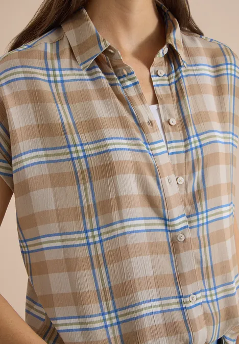 Nahe Aufnahme einer beige-karierten Kurzarmbluse mit blauen und weißen Streifen.