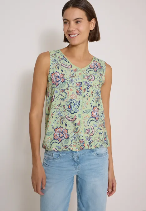 Blusentop mit V-Neck und Print raw matcha lime Eine junge Frau trägt ein ärmelloses, grünes Top mit Blumenmuster und helle Jeans vor weißer Wand.