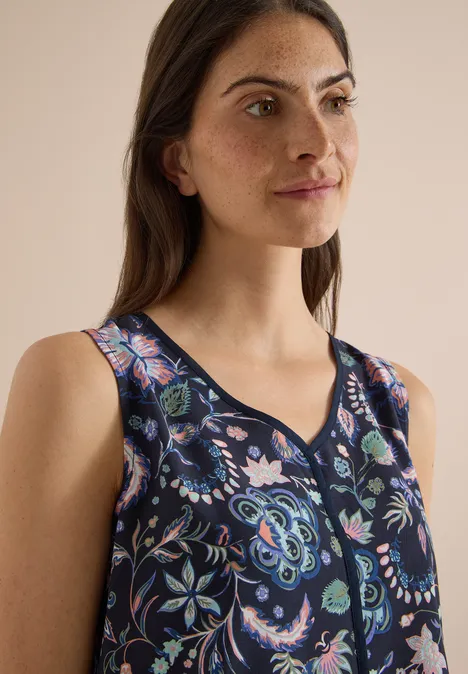 Frau im Porträt, trägt ärmelloses, dunkelblaues Top mit buntem Blumenmuster