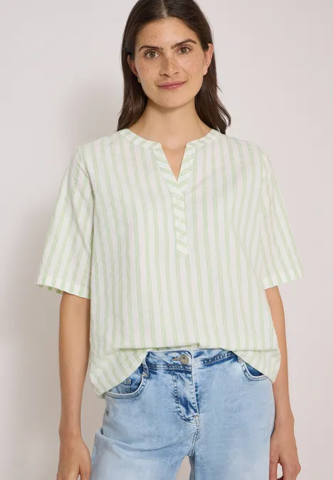 Halbarm Bluse mit Split Neck und Streifen raw matcha lime Frau trägt helle, grün-weiße Bluse mit Streifen und helle Jeans vor neutralem Hintergrund
