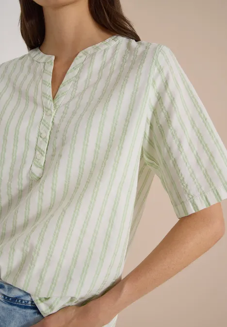Halbarm Bluse mit Split Neck und Streifen raw matcha lime Frau in locker geschnittener, hellgrün-weiß gestreifter Bluse mit kurzen Ärmeln, lässig in Jeans gesteckt.