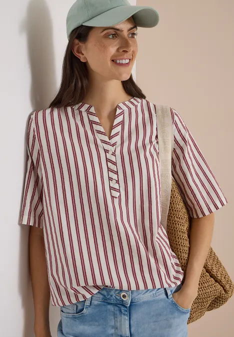Halbarm Bluse mit Split Neck und Streifen russet red Junge Frau mit grüner Mütze, rot-weiß gestreiftem Hemd und Basttasche, lächelnd und entspannt.