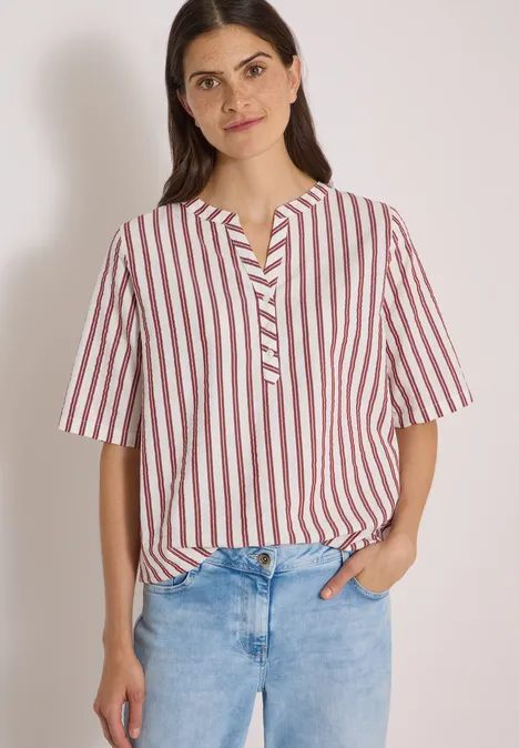 Halbarm Bluse mit Split Neck und Streifen russet red Frau in gestreiftem rot-weißem Blusenshirt und blauen Jeans vor hellem Hintergrund.