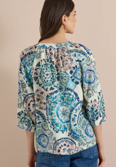 Frau von hinten in Bluse mit mandalaartigem blau-beigem Muster.