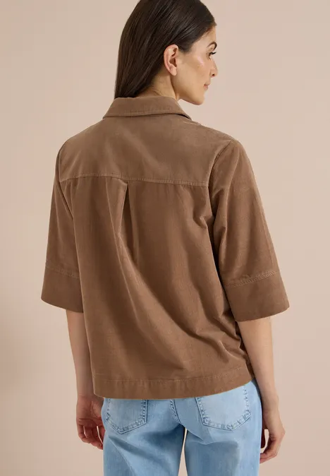 Chemisier à manches courtes en velours côtelé avec poche poitrine creamy mocha Rückansicht einer Frau in braunem Cord-Hemd und hellen Jeans vor neutralem Hintergrund.