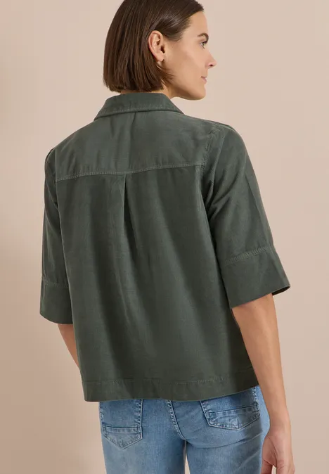 Frau von hinten, trägt grüne Cord-Hemdjacke mit Ellbogenärmeln und blaue Jeans.