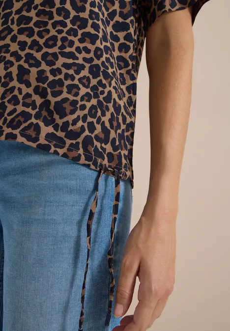 Nahaufnahme eines Unterkörpers in blauer Jeans und Leopardenmuster-Bluse mit seitlichen Schnürungen