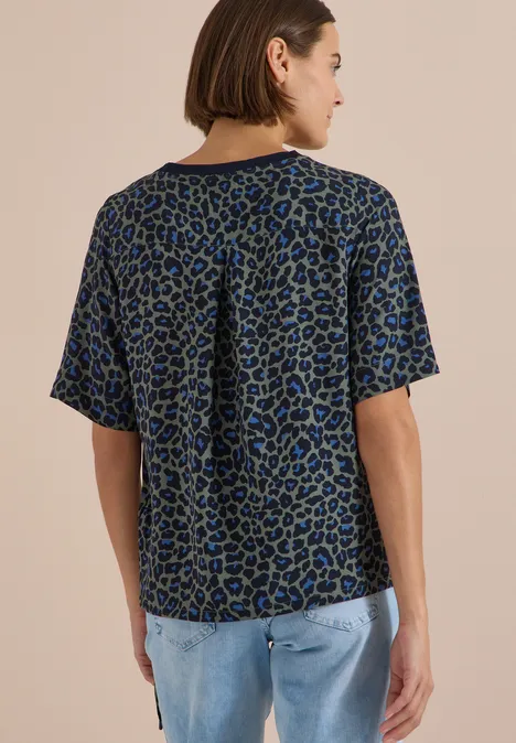 Frau von hinten in lockerem, kurzärmeligem Shirt mit blau-schwarzem Animal-Print und Jeans.