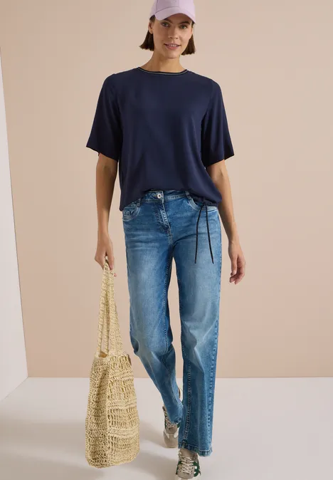 Kurzarm Blusenshirt mit Rundhals urban dark blue Frau in lässigem Outfit: dunkelblaues T-Shirt, Jeans, weiße Sneaker, Strohtasche und rosa Cap.