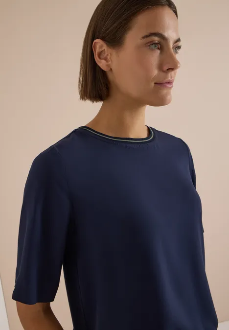 Kurzarm Blusenshirt mit Rundhals urban dark blue Eine Frau in Seitenansicht trägt ein dunkelblaues, kurzärmeliges Oberteil mit mehrfarbigem Kragen.