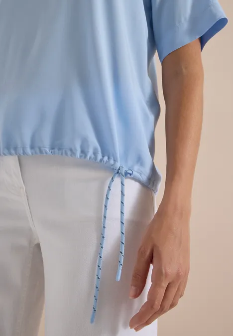 Kurzarm Blusenshirt mit Rundhals easy blue Nahaufnahme eines hellblauen Oberteils mit Kordelzug und einer weißen Hose.