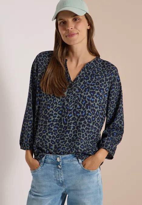 Tunique léopard à manches 3/4 et col fendu dried olive green Frau trägt blaue, gemusterte Bluse, Jeans und weiße Kappe