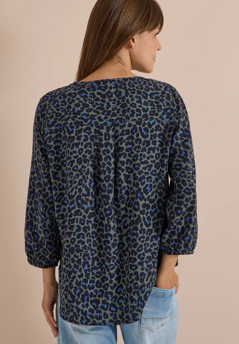 Tunique léopard à manches 3/4 et col fendu dried olive green Frau von hinten in locker sitzender Bluse mit blau-grünem Leopardenmuster und hellen Jeans.