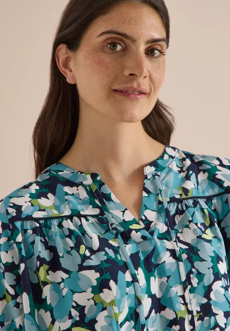 3/4-Arm Tunika mit Split Neck und Print urban dark blue Porträt einer Frau mit dunklen Haaren und blauer Blumenbluse vor hellem, neutralem Hintergrund.