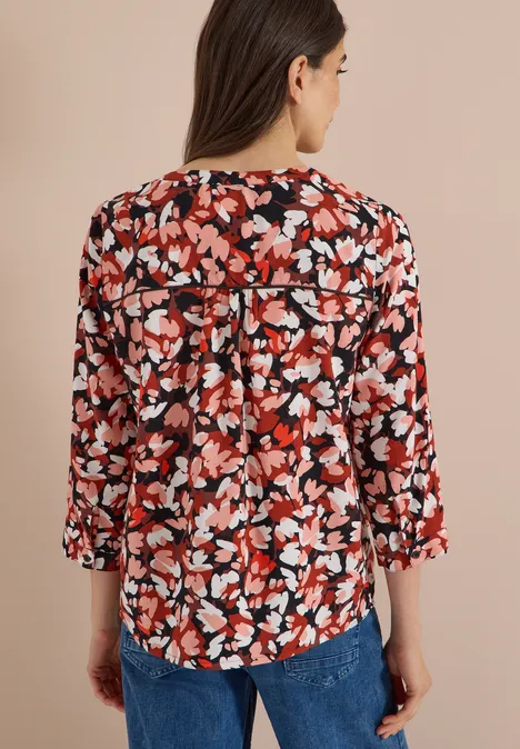 3/4-Arm Tunika mit Split Neck und Print russet red Frau von hinten in einer blumigen Bluse mit Rot-, Weiß- und Schwarztönen, 3/4-Ärmel, trägt blaue Jeans.