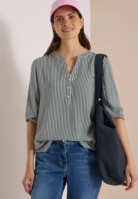 3/4-Arm Bluse mit Split Neck und Streifen khaki Frau in grün-weiß gestreifter Bluse, Jeans, rosa Cap und Umhängetasche, stehend und lächelnd.