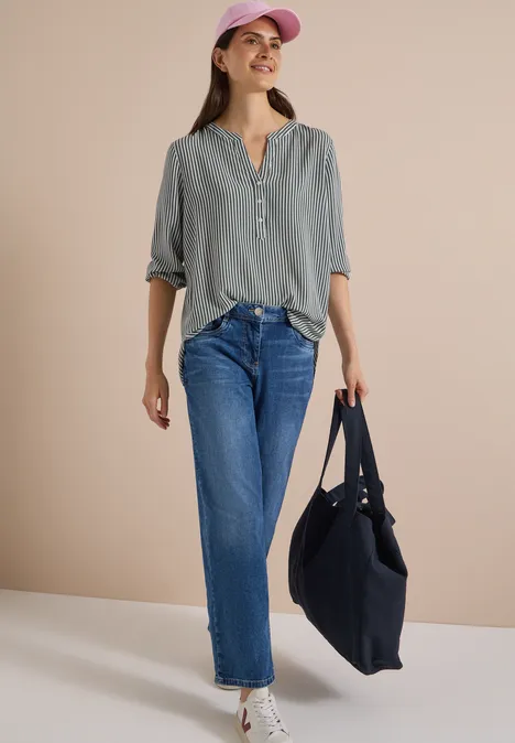 3/4-Arm Bluse mit Split Neck und Streifen khaki Frau in grauem Oberteil, blauen Jeans, rosa Mütze und schwarzer Tasche vor beigem Hintergrund.