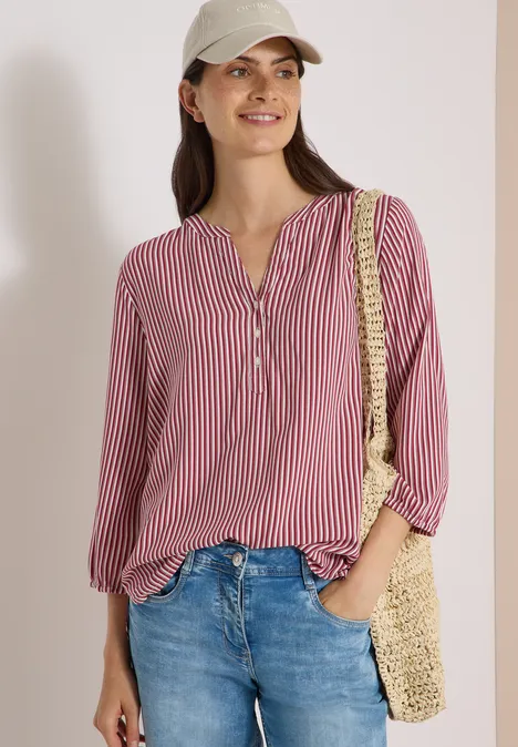 3/4-Arm Bluse mit Split Neck und Streifen russet red Frau mit roter, gestreifter Bluse, Jeans, Strohtasche und Cap, lächelnd vor weißem Hintergrund.