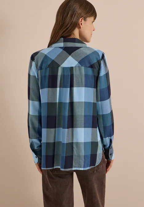 Vue de dos d’une femme portant une chemise à carreaux bleus et verts et un pantalon marron.
