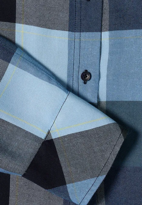 Gros plan sur une chemise à carreaux bleu et gris avec patte de boutonnage.
