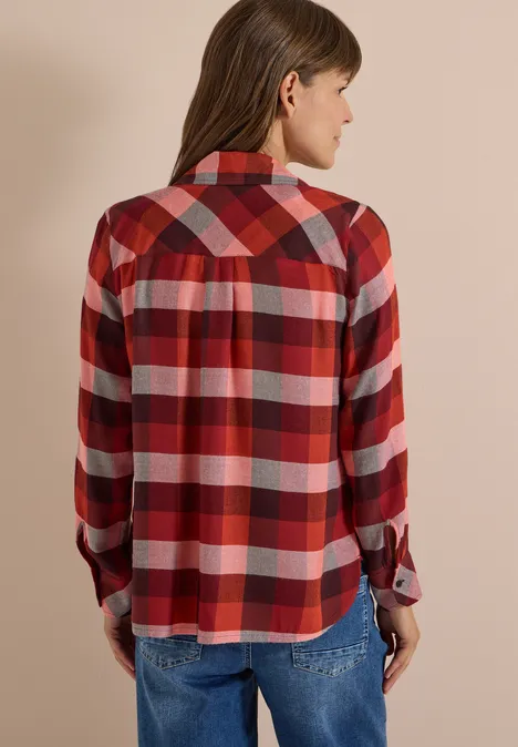 Femme de dos portant une chemise à carreaux rouges et un jean sur fond neutre.