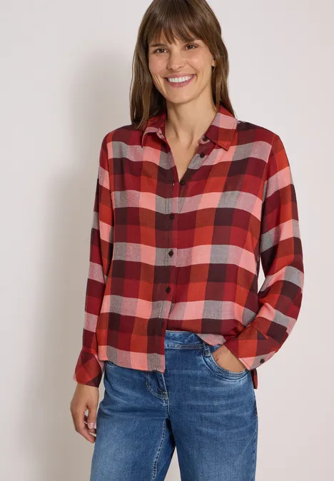 Une femme souriante porte une chemise à carreaux rouges et blancs avec un jean.