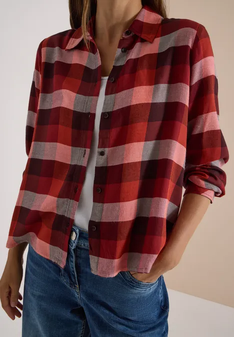 Personne porte une chemise à carreaux rouge sur un top blanc et un jean bleu.